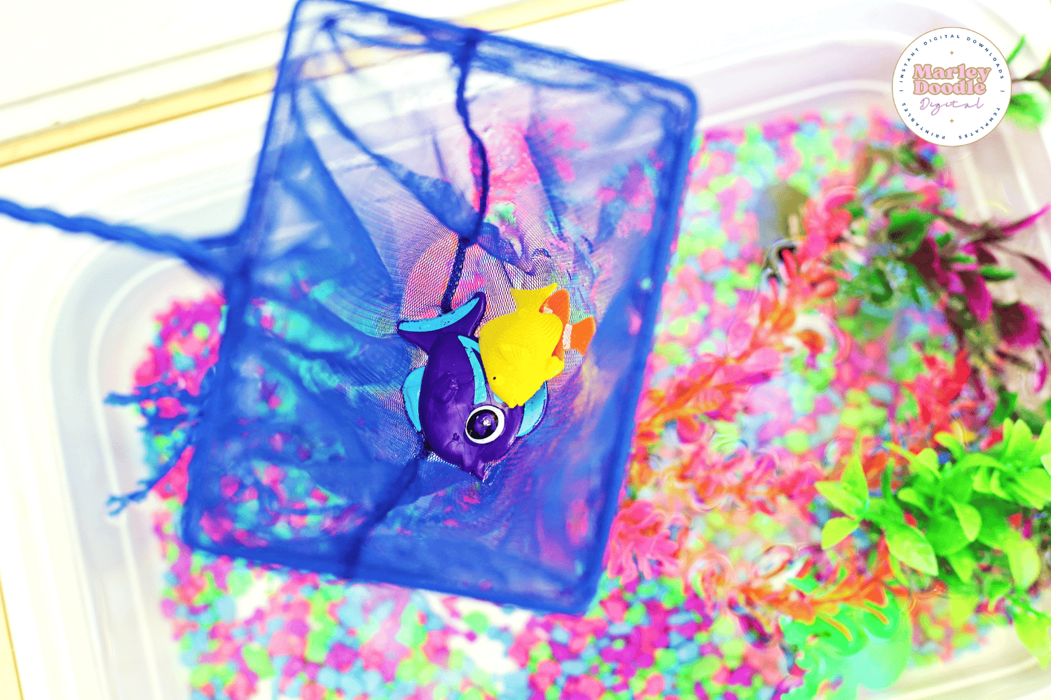 Toy fish in a net inside vibrant aquarium sensory bin.