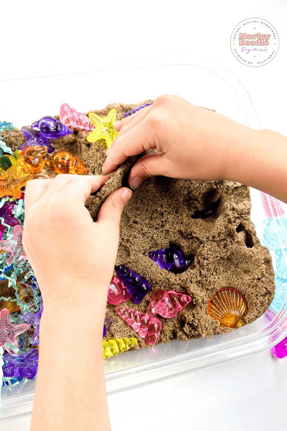 Child exploring colorful seashell toys in a sensory bin filled with sand.